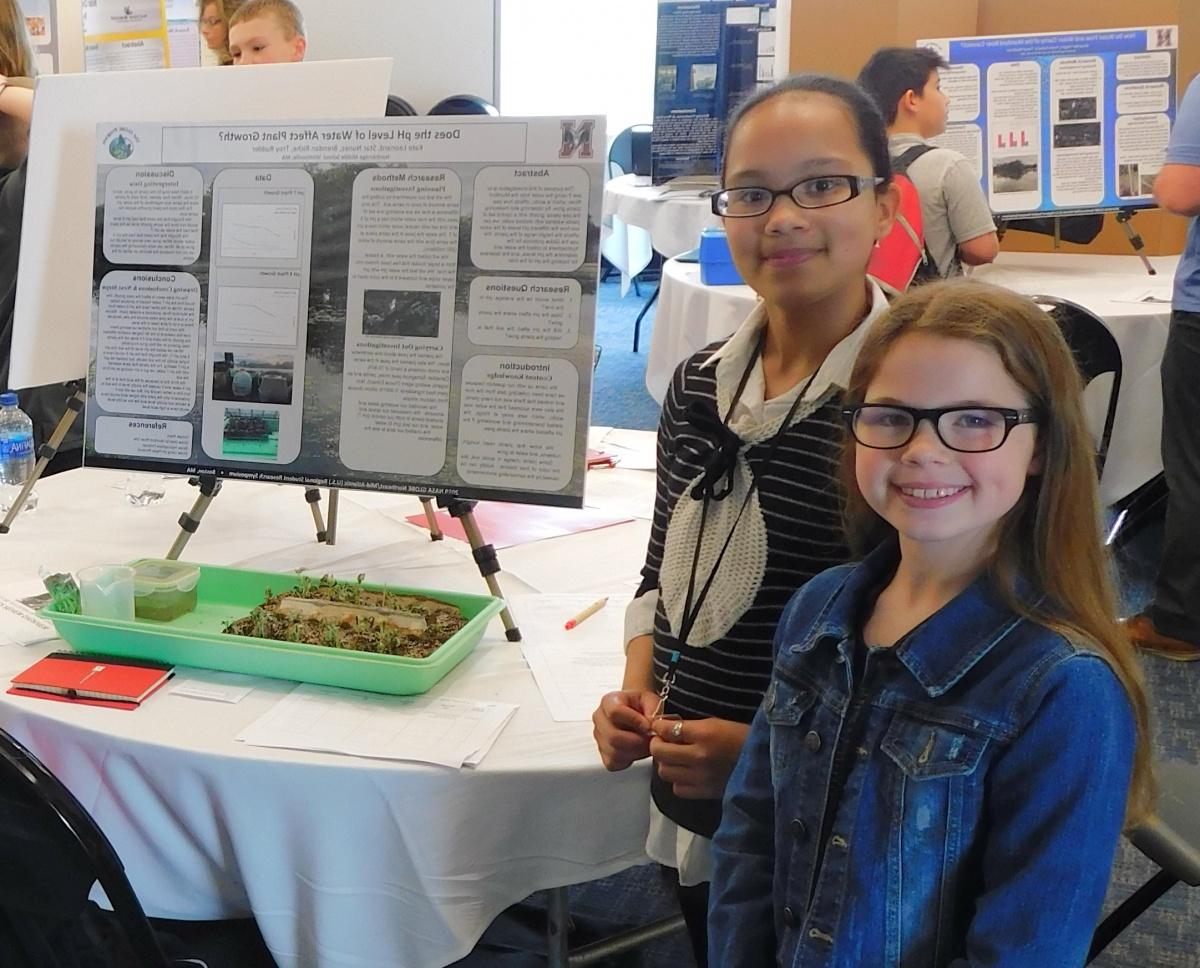 Two middle school girls stand beside a scientific poster, smiling